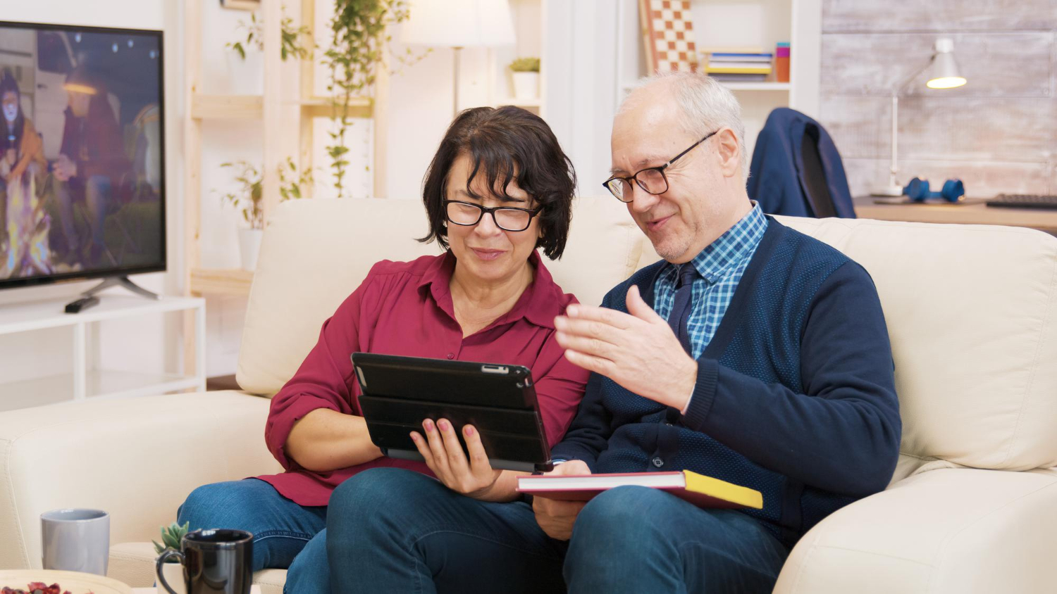 old-couple-sitting-on-sofa-during-video-call-on-tablet-old-couple-waving-at-tablet